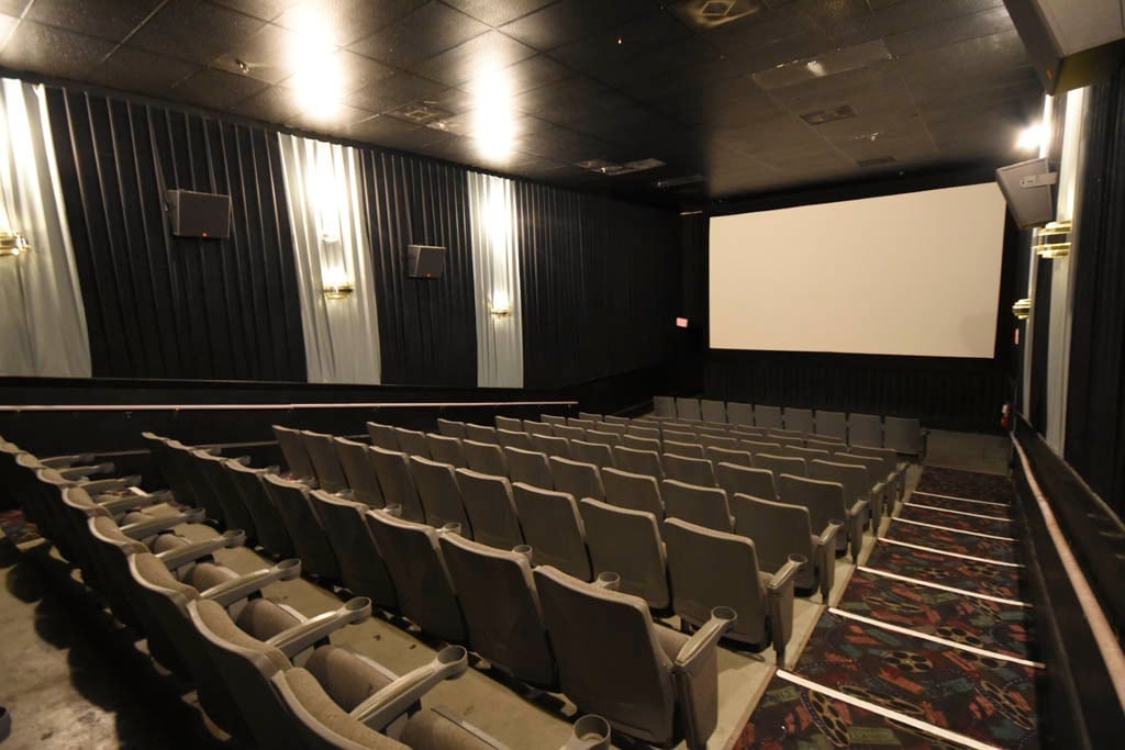 photo from back of auditorium showing rows of theater chairs & white screen in the front