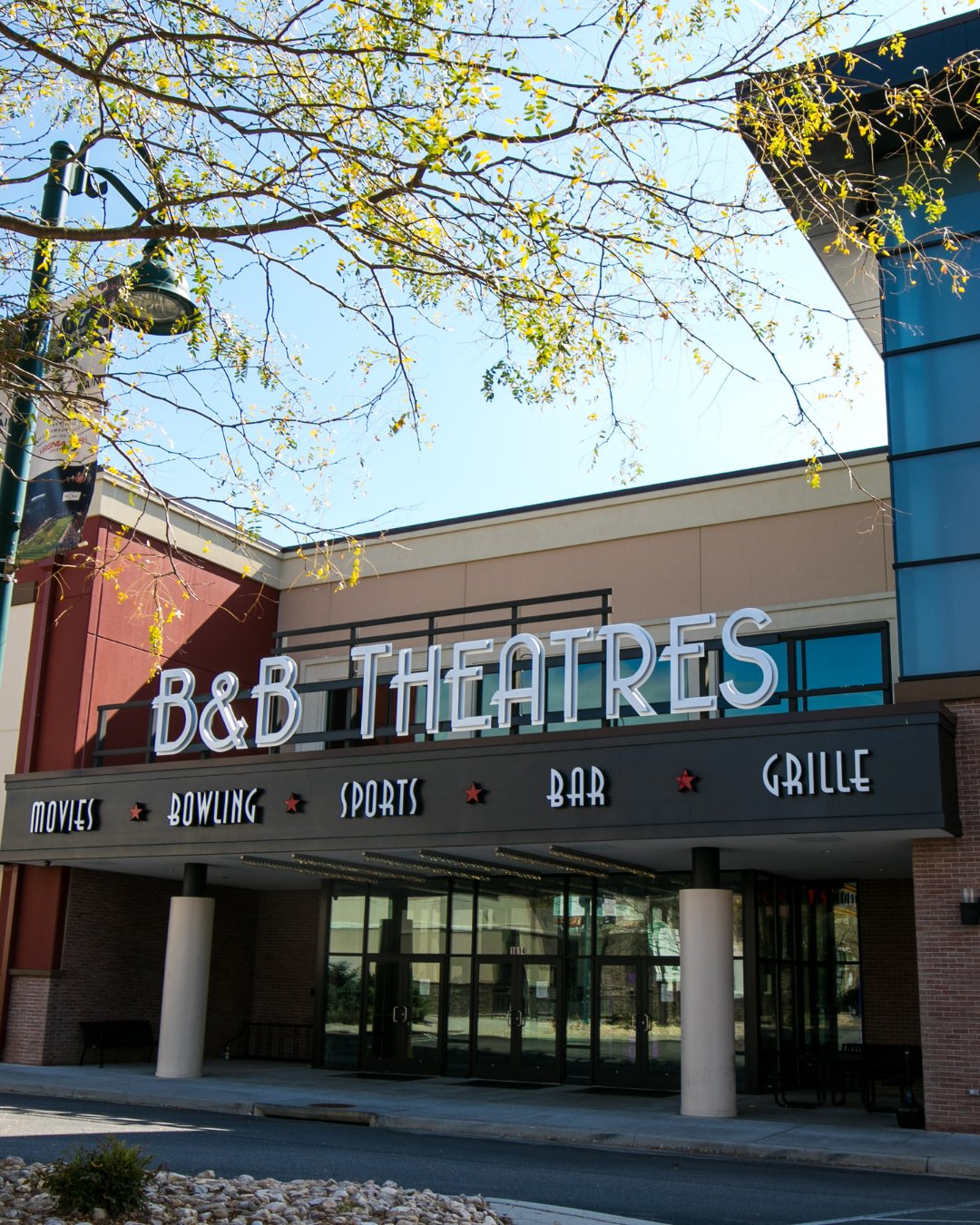 exterior of building in daytime. Signage reads "B&B Theatres" and underneath that smaller reads "MOVIES BOWLING SPORTS BAR GRILLE"