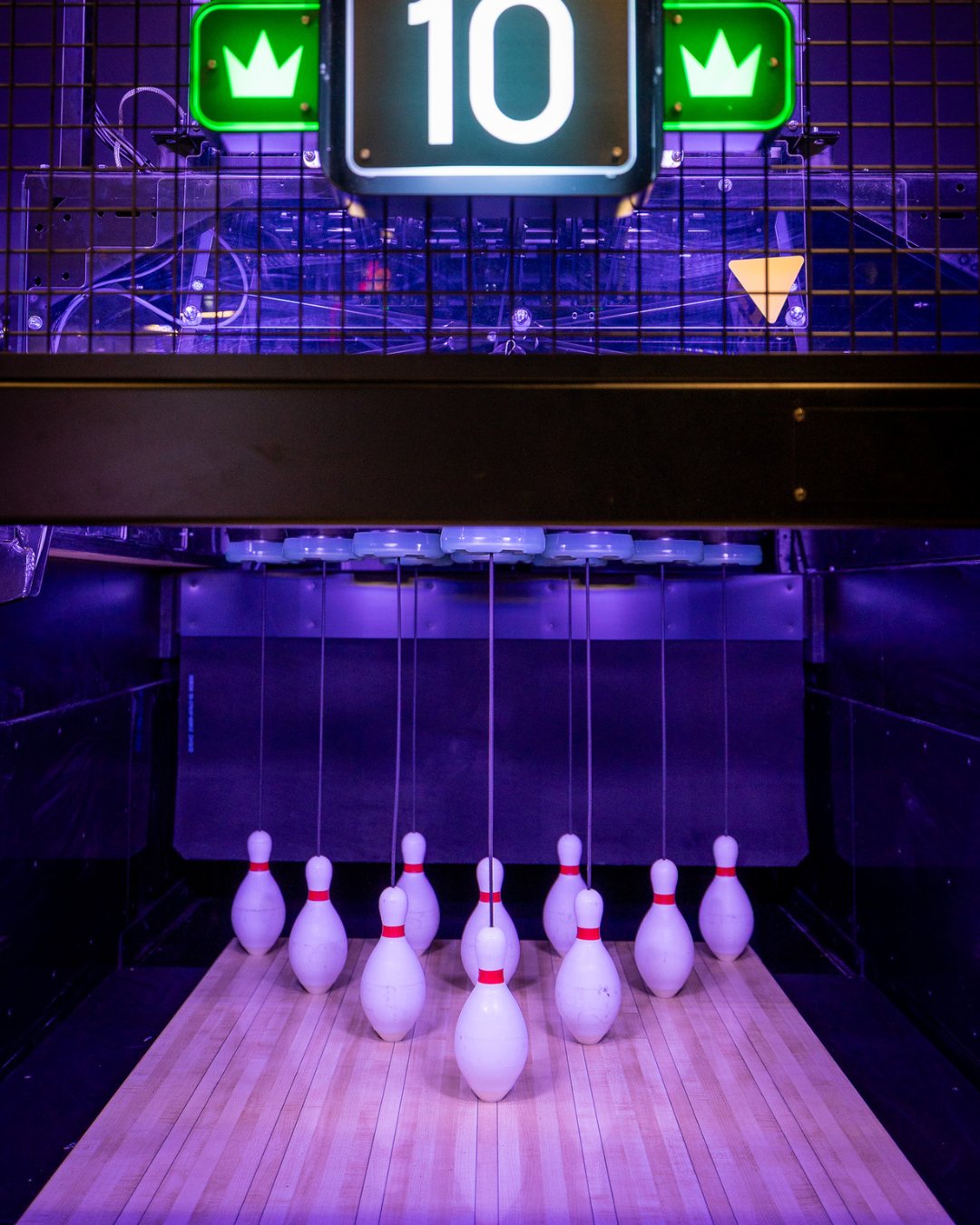 bowling ball stand in the center. in the background bowling lanes & tvs. surrounded by seating on the outer edges