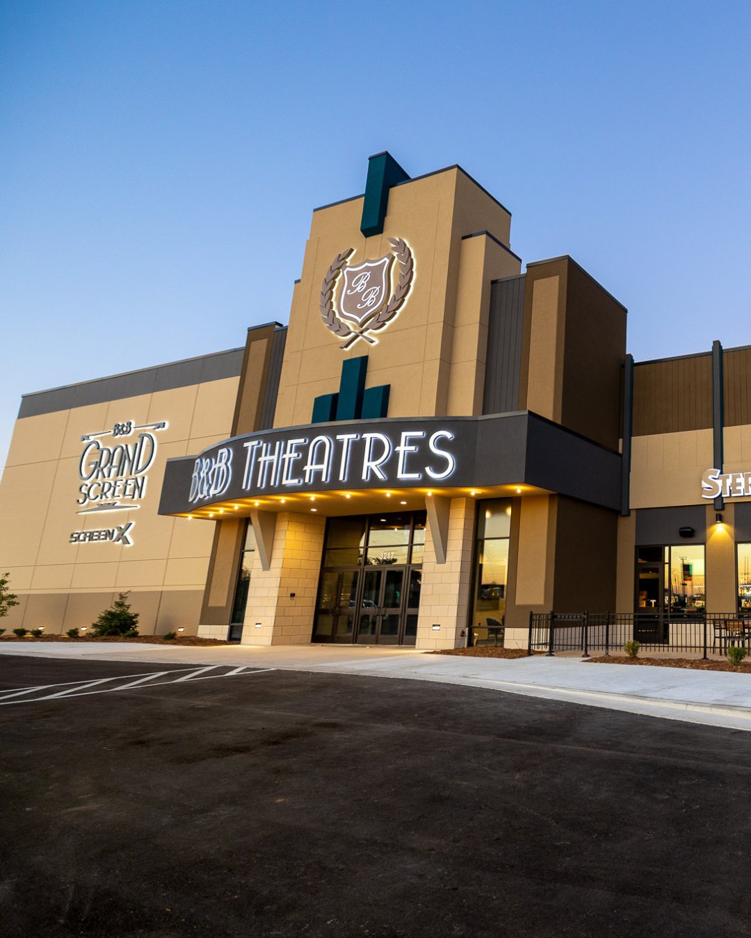 exterior shot of entrance during sunset. Lit signage on the build reads "B&B Theatres" B&B Grand Screen ScreenX. Near the top of teh building is a B&B Crest