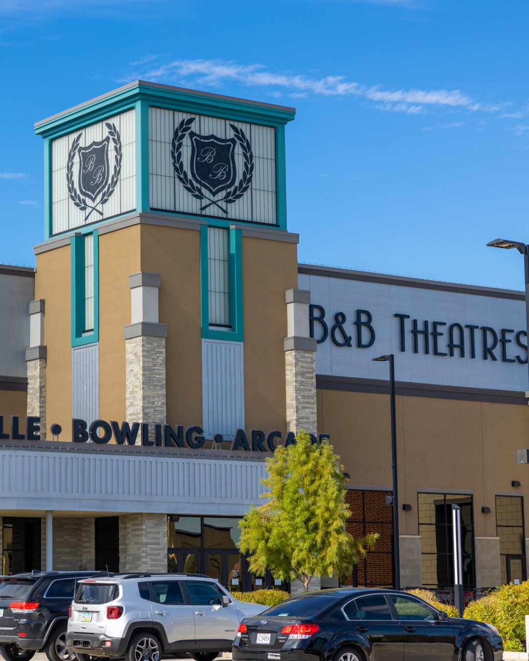 Exterior of ankeny in daytime. Top tower features 2 B&B crests. To the right side is a sign that reads "B&B Theatres" In the front are a couple of vehicles in parking spots