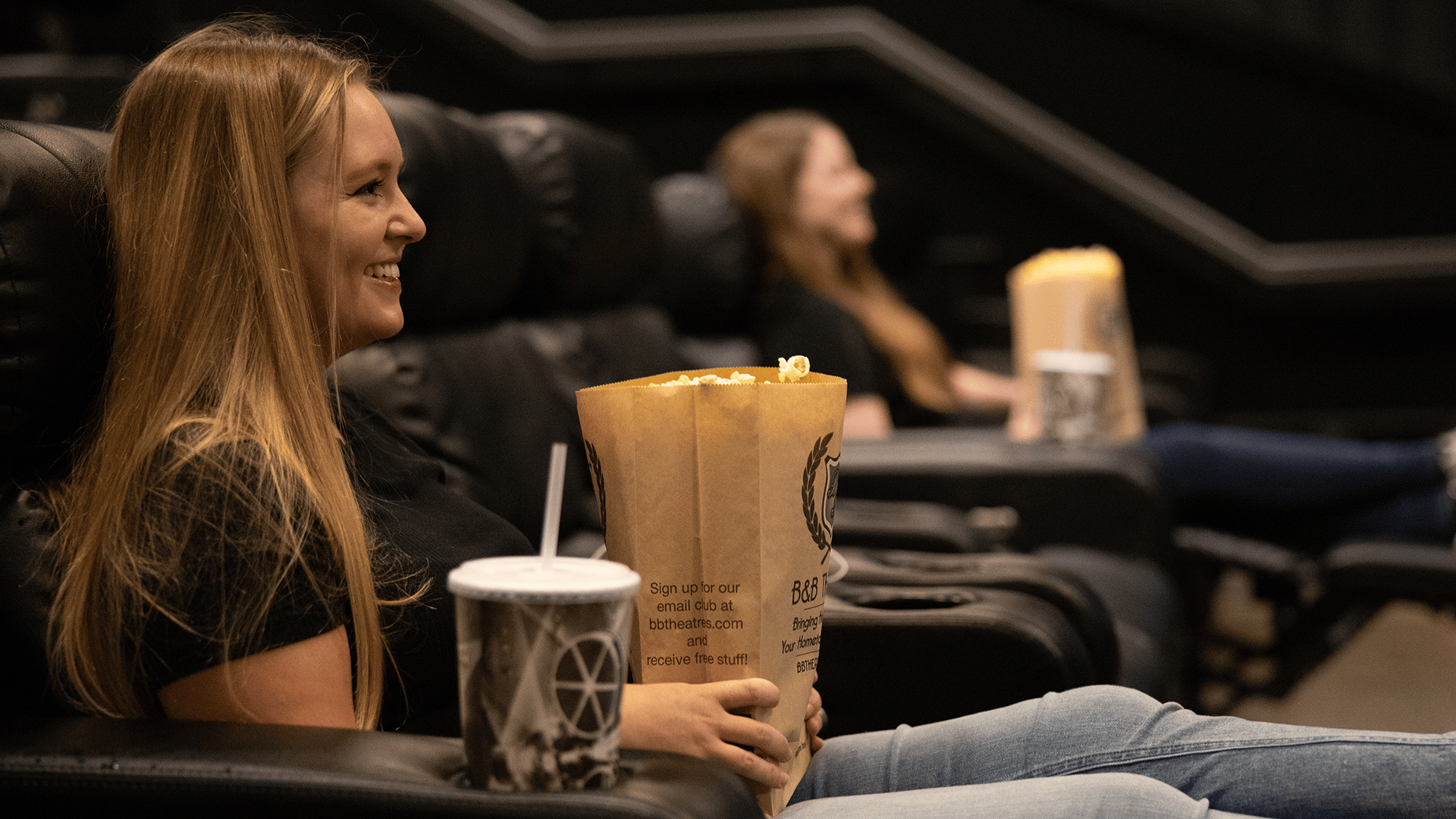 guests holding popcorn sitting in recliners facing screen