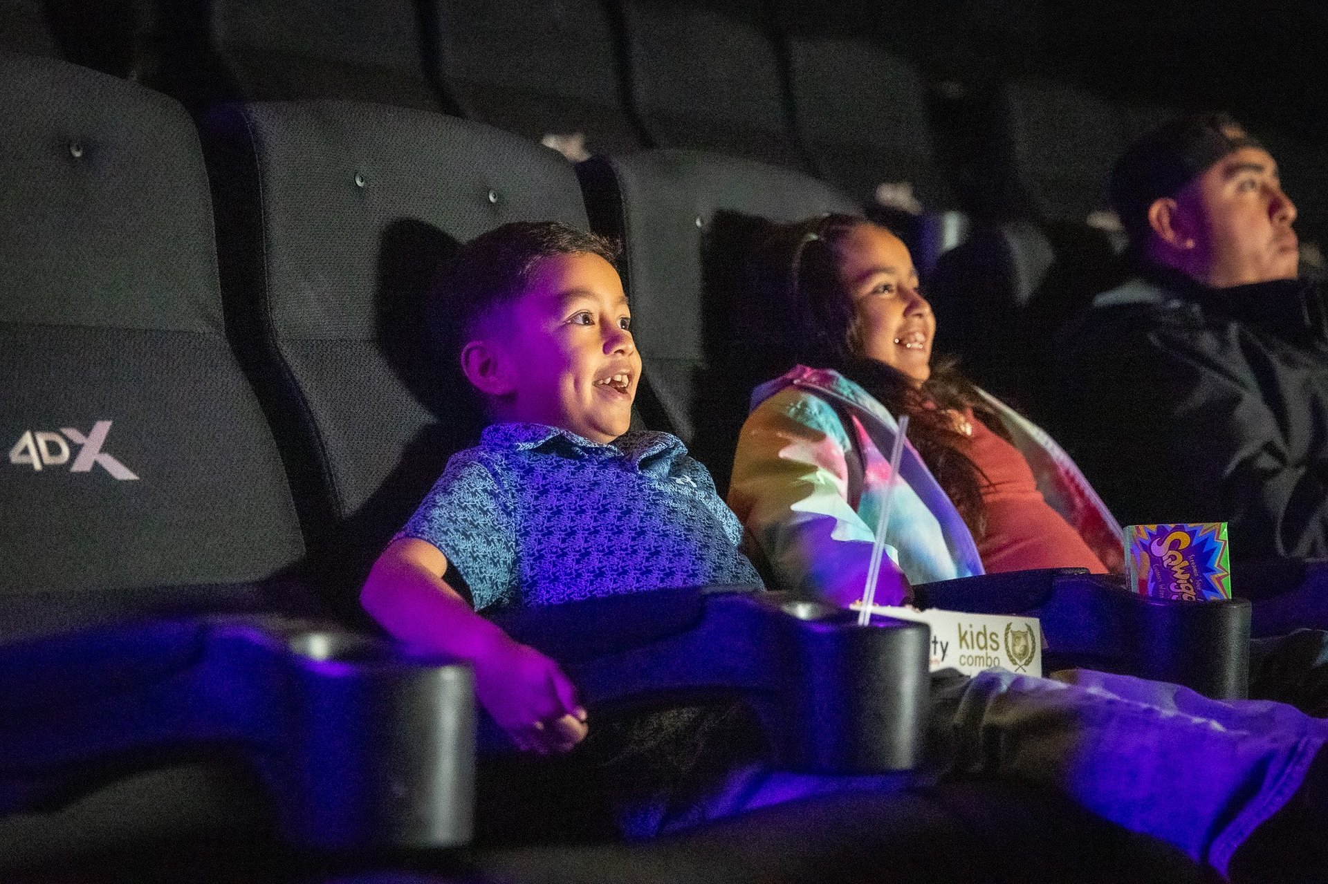 young boy and girl sitting in black chairs. Both are smiling & wide-eyed with excitement