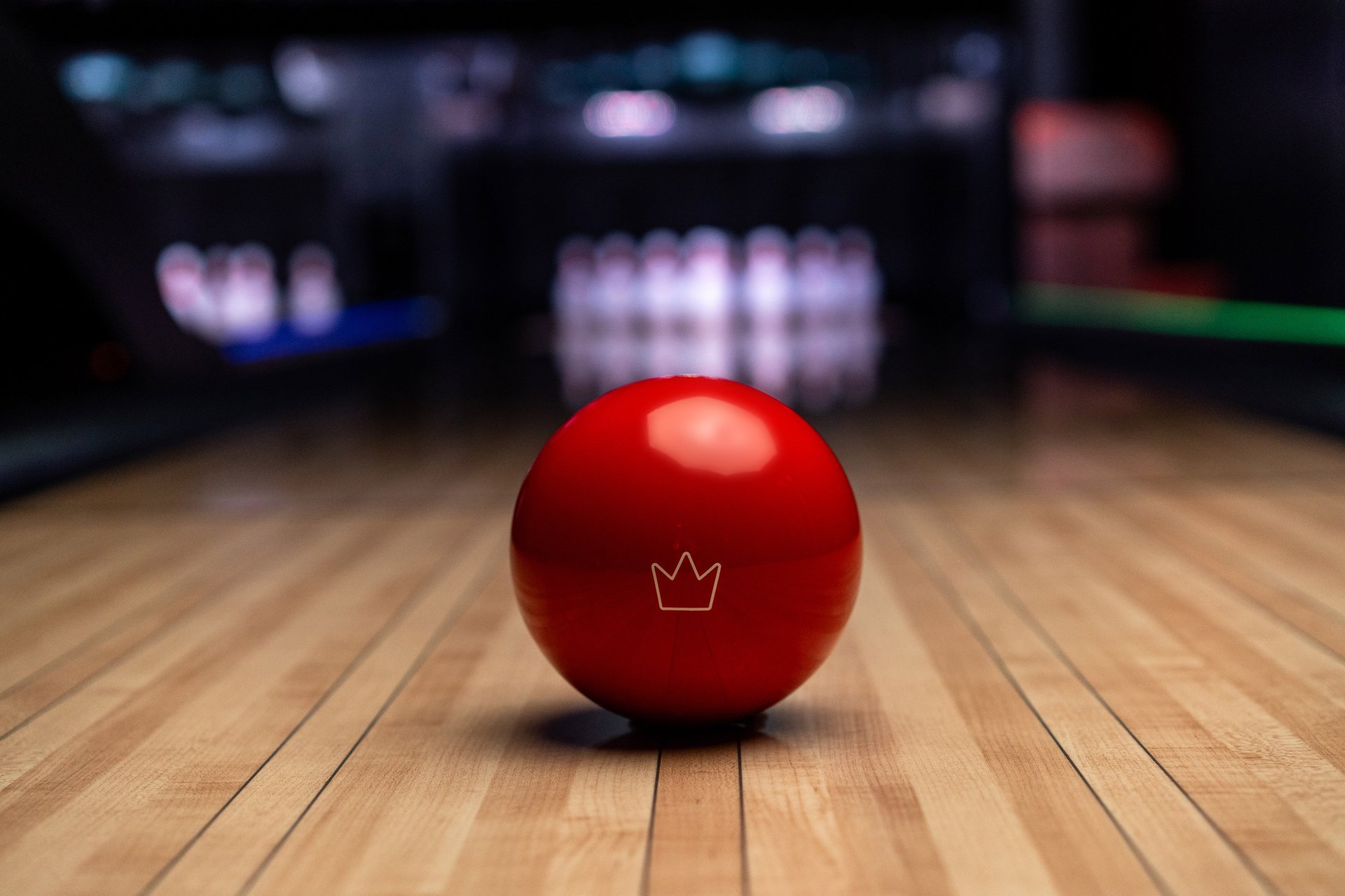small red duckpin ball sitting on lane in the foreground. pins in the background