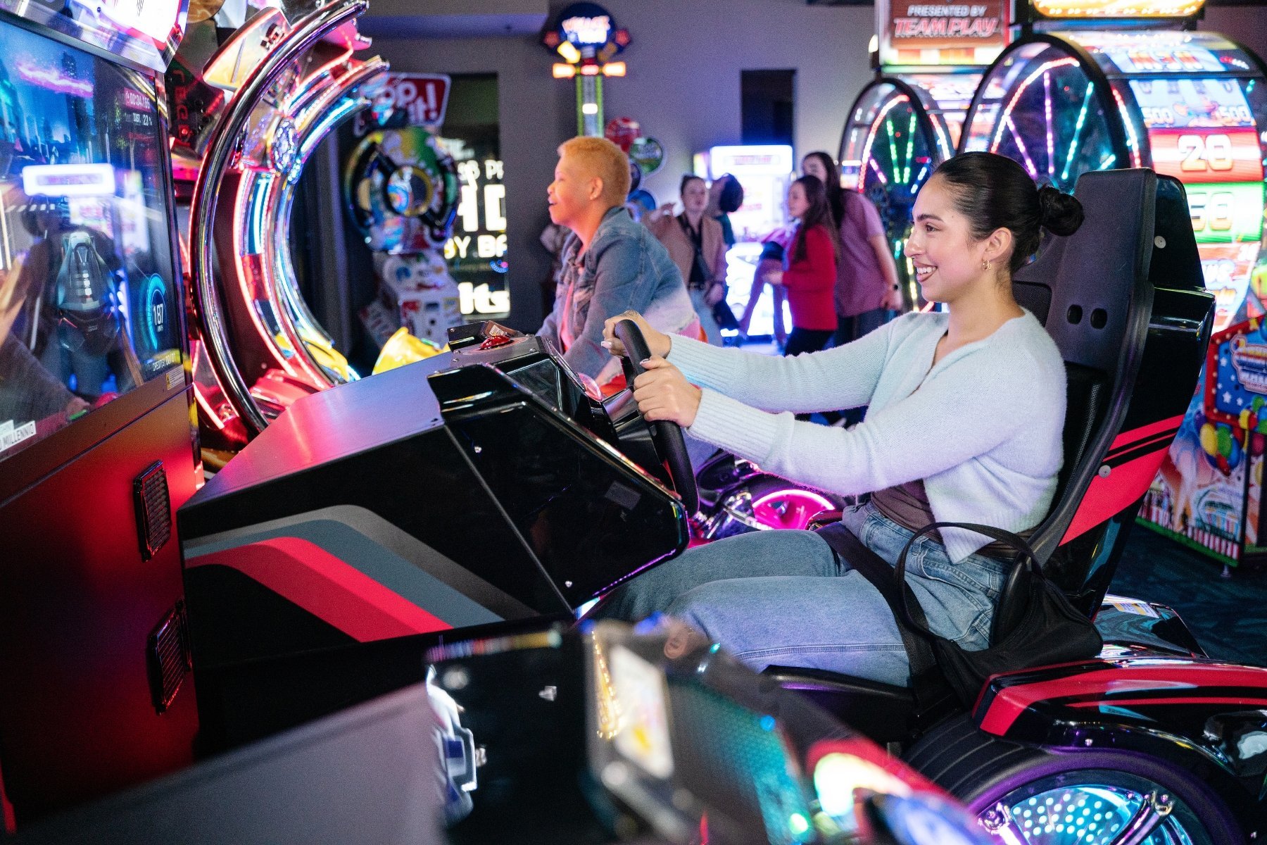 woman sitting in a racing car arcade game with her hand on the steering wheel.