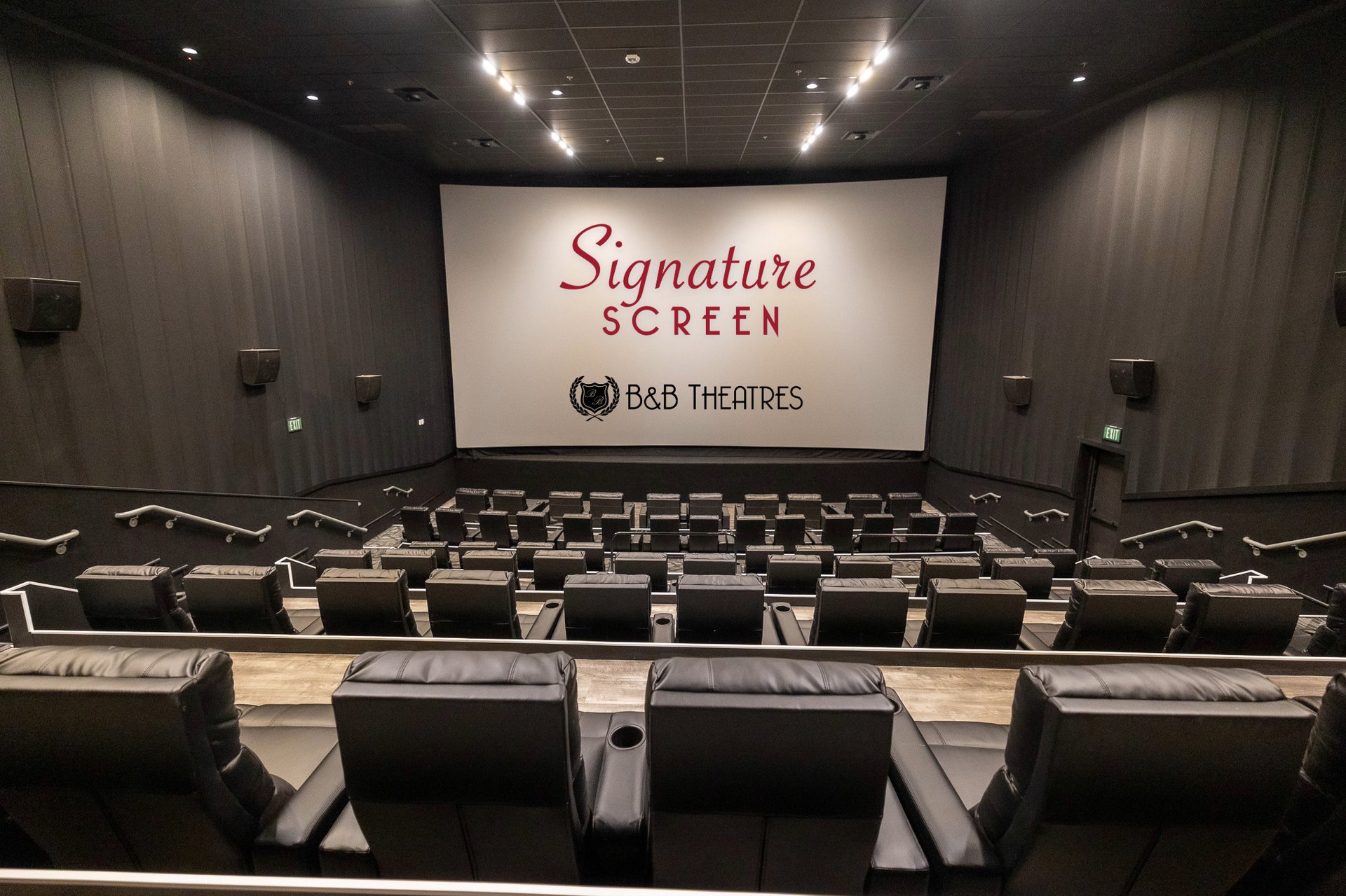 picture from the back of an auditorium. Lights are on. Screen has 2 logos on it that reads Signature Screen B&B Theatres