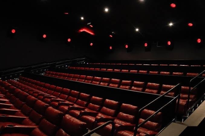 A modern movie auditorium with soft lighting and rows of plush red recliner seats arranged in a clean, stadium-style layout.