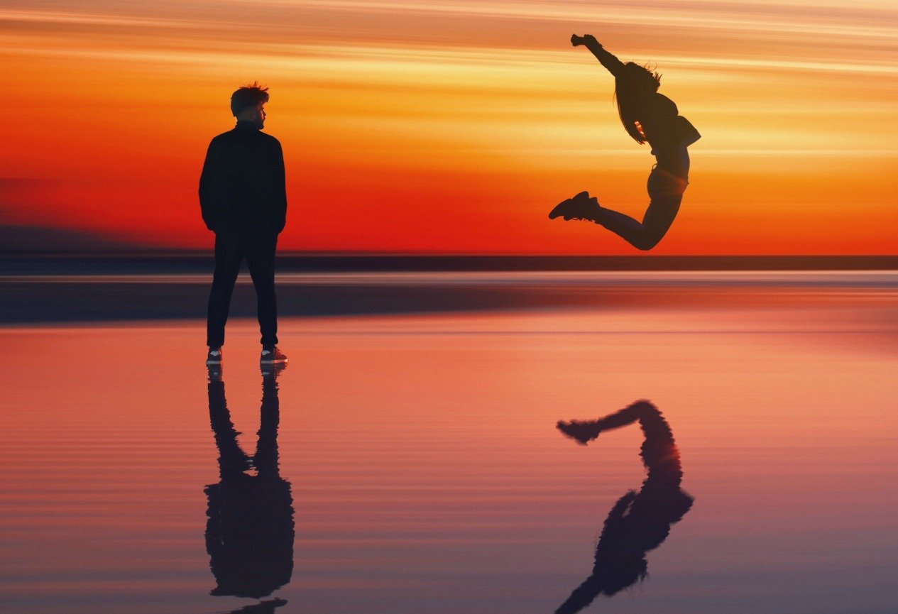 two people on beach with sunset behind them. One person jumping in air