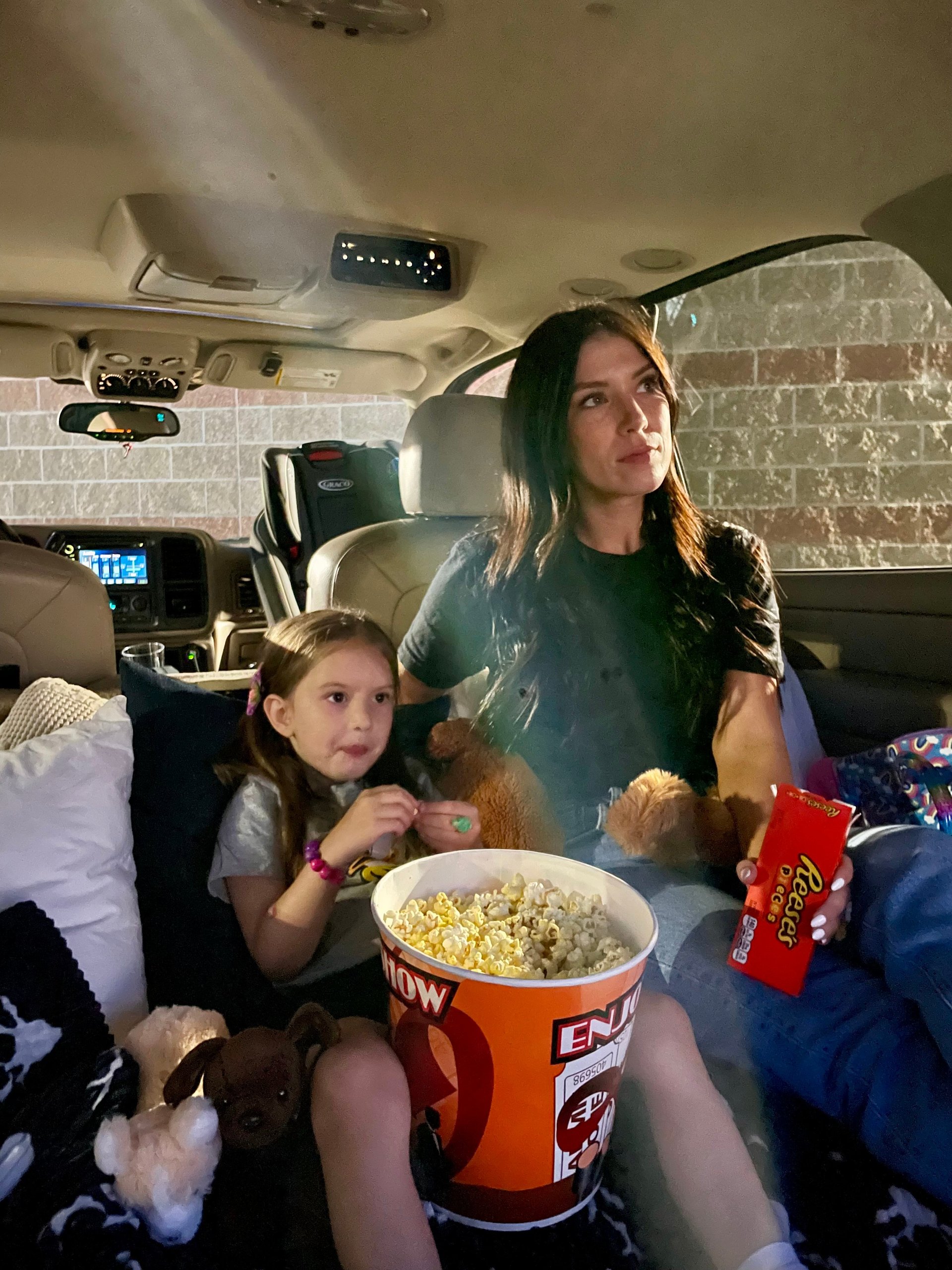 mother and daughter watching a drive-in movie from the back of an SUV