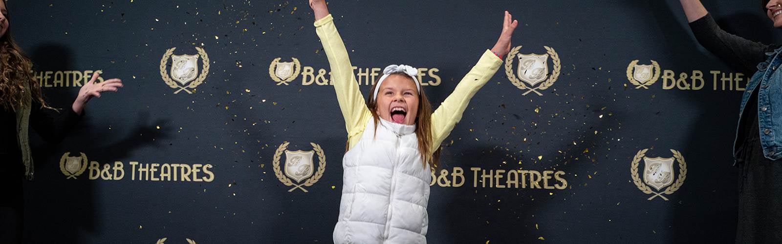 young girl with her hands in the air in front of a b&b theatres sign