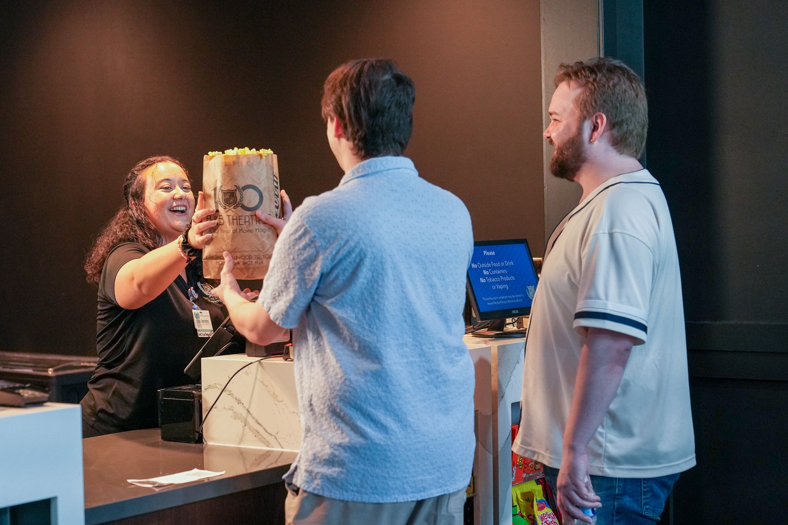 employee smiling and handing a large bag of popcorn to 2 guests.