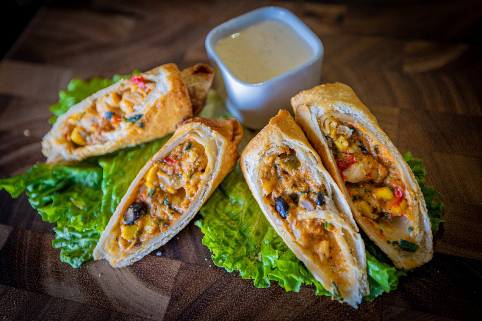 butcher block background. 4 sliced southwest egg rolls fanned out sitting on top of 2 leaves of lettuce. small square container holding ranch placed behind the egg rolls.