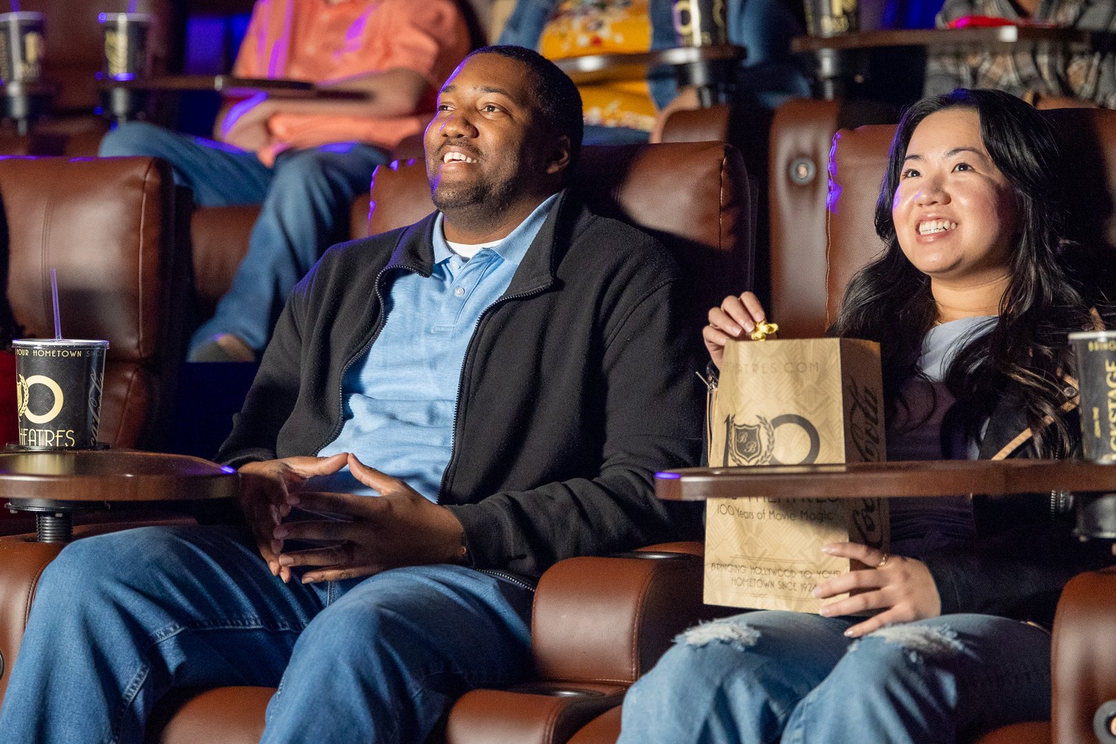 man & woman sitting in recliners. both are smiling. Woman is holding a bag of popcorn