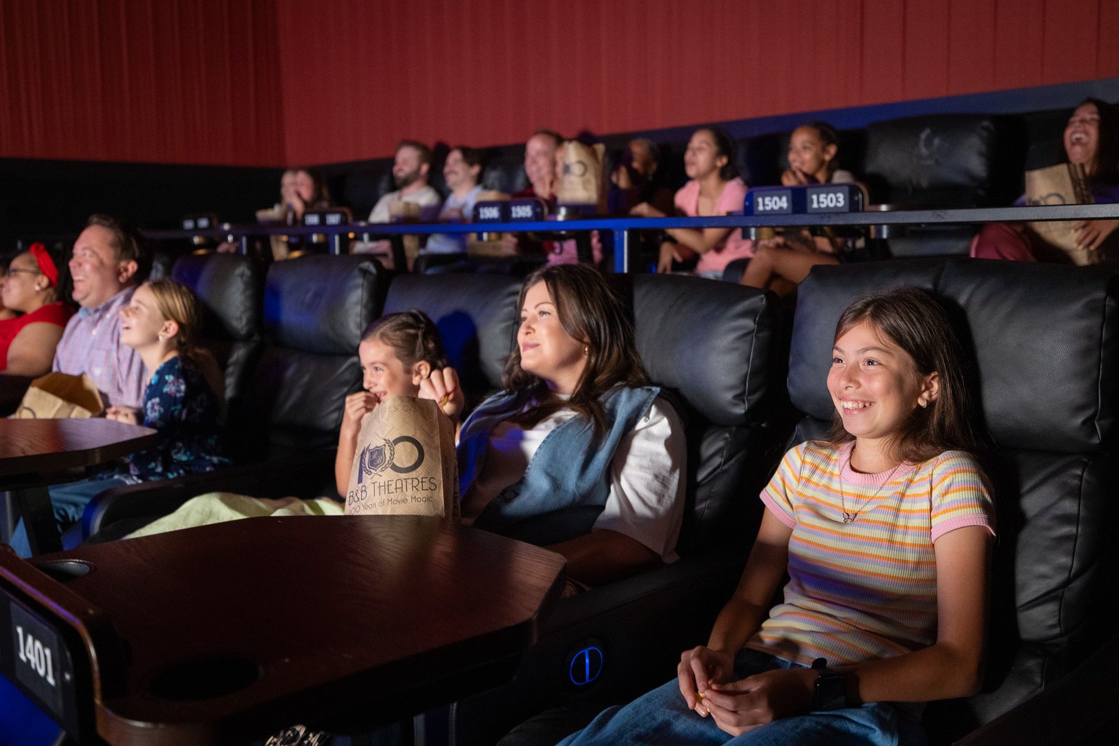 full auditorium of adults & kids. they are smiling, some are holding popcorn