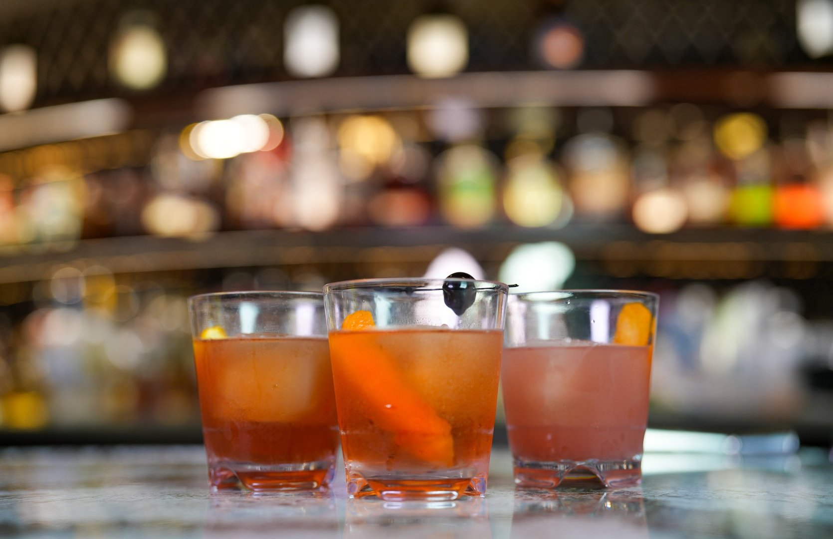 3 old fashioned drinks sitting on the bar. they vary slightly in color, but look mostly the same.