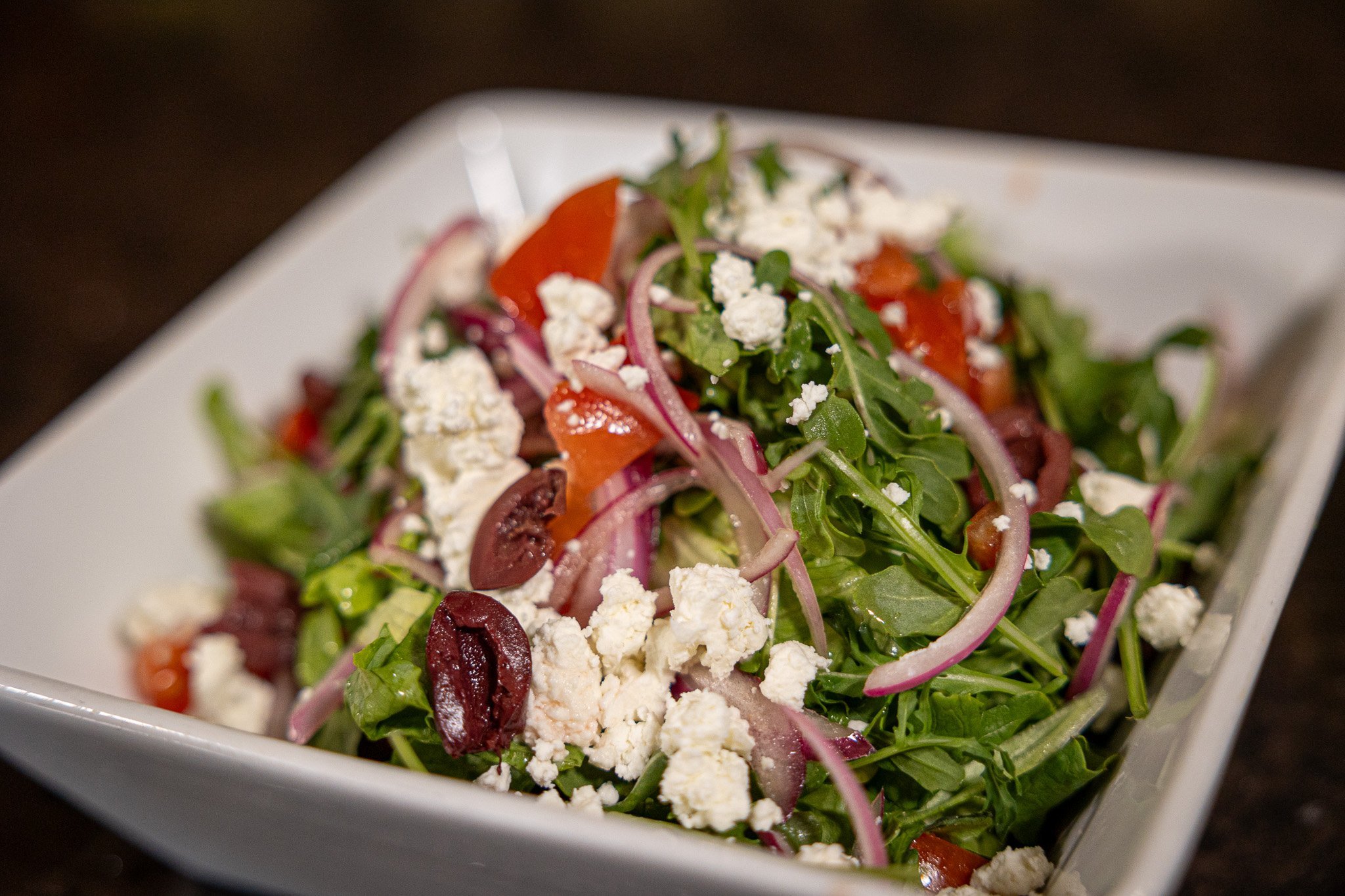 greek arugula salad topped with feta cheese, olive, tomato, onions