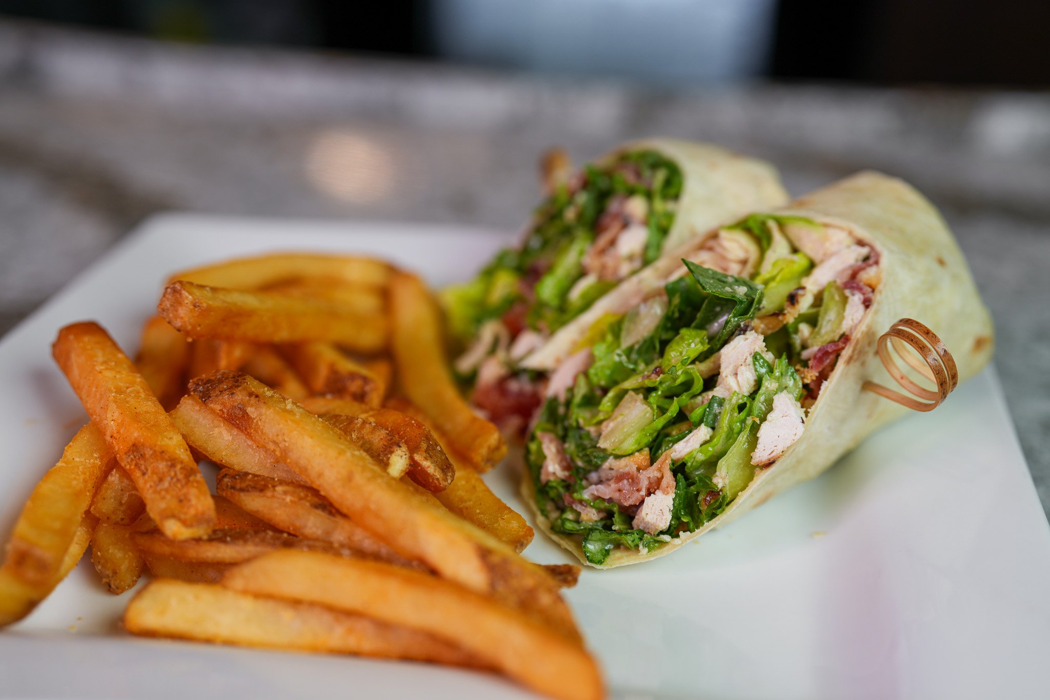 plate of chicken caesar wrap cut in half with a side of seasoned fries