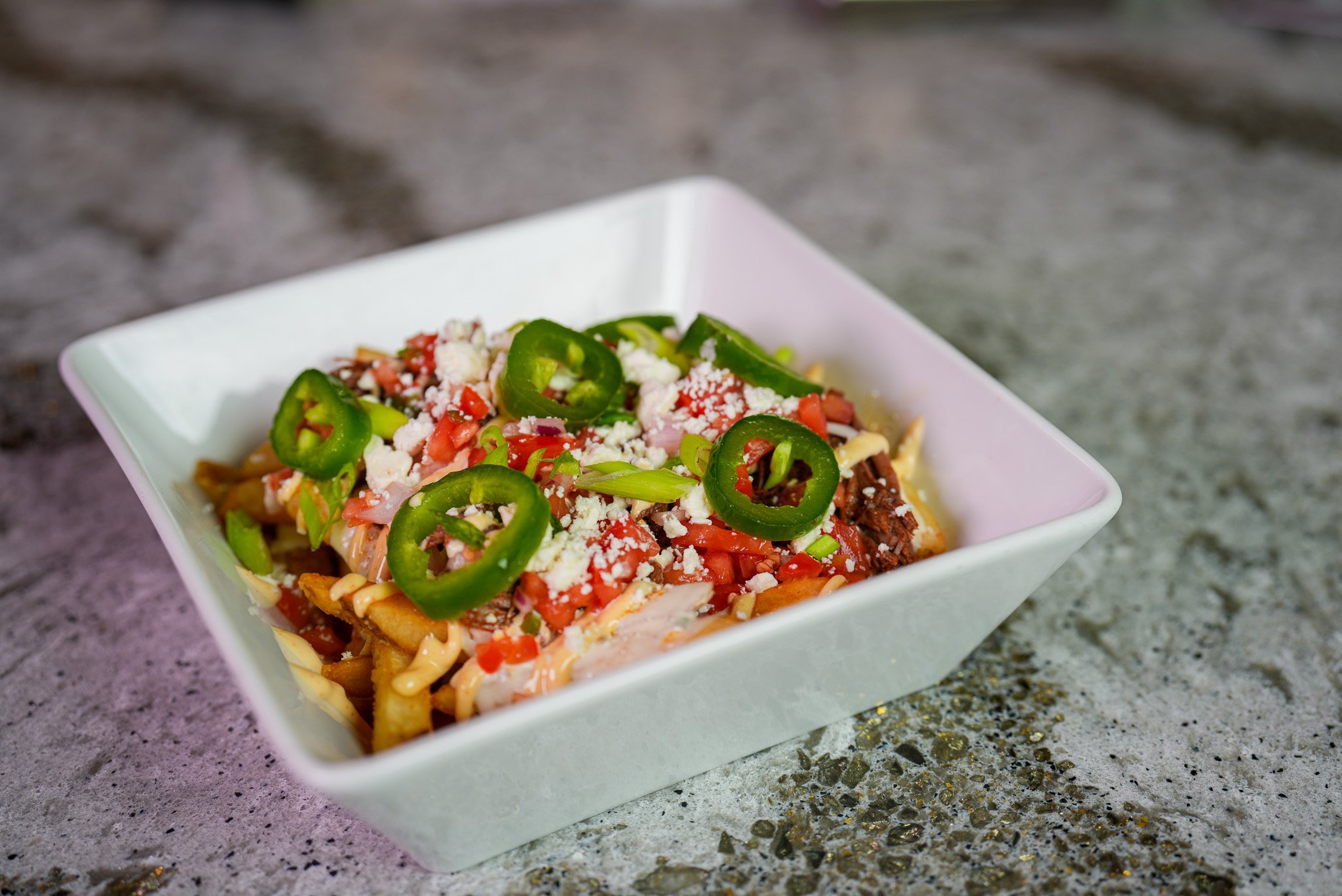 bowl of loaded fries topped with birria beef, cheese sauce, tomatoes, jalapenos and crumbled cheese