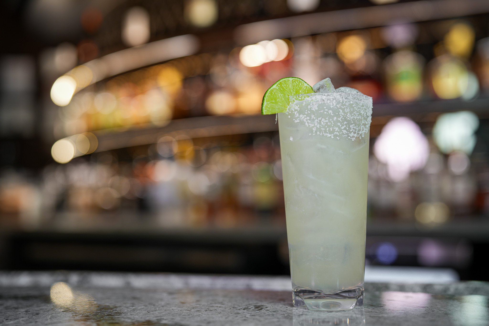 tall glass of ice cold margarita garnished with a lime wedge and salt rim