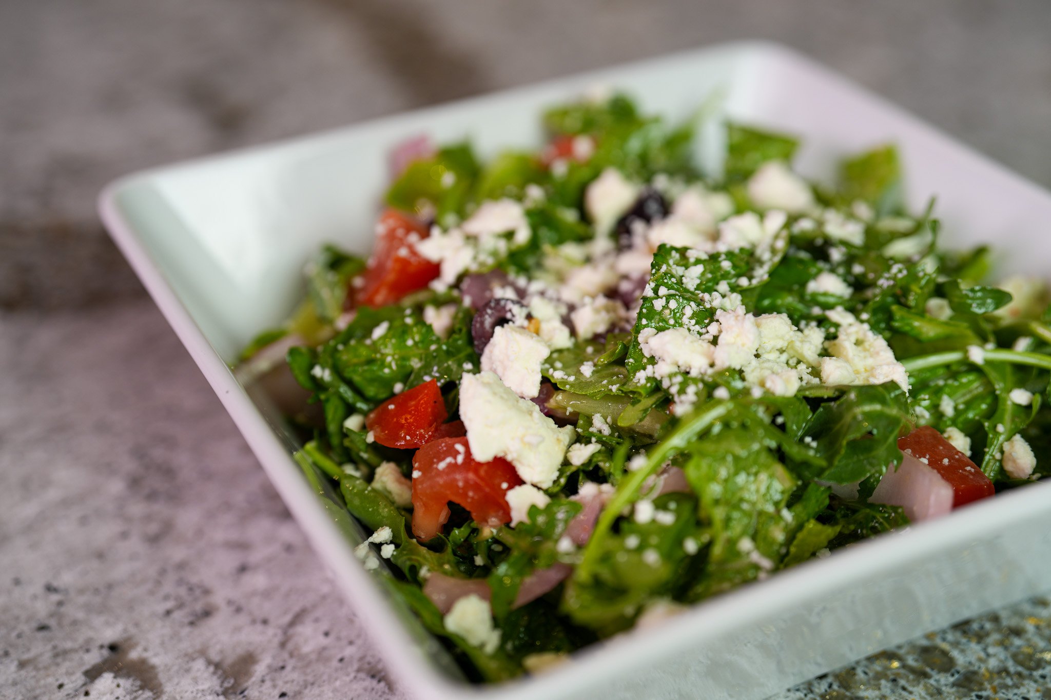 greek arugula salad topped with feta cheese, olive, tomato, onions