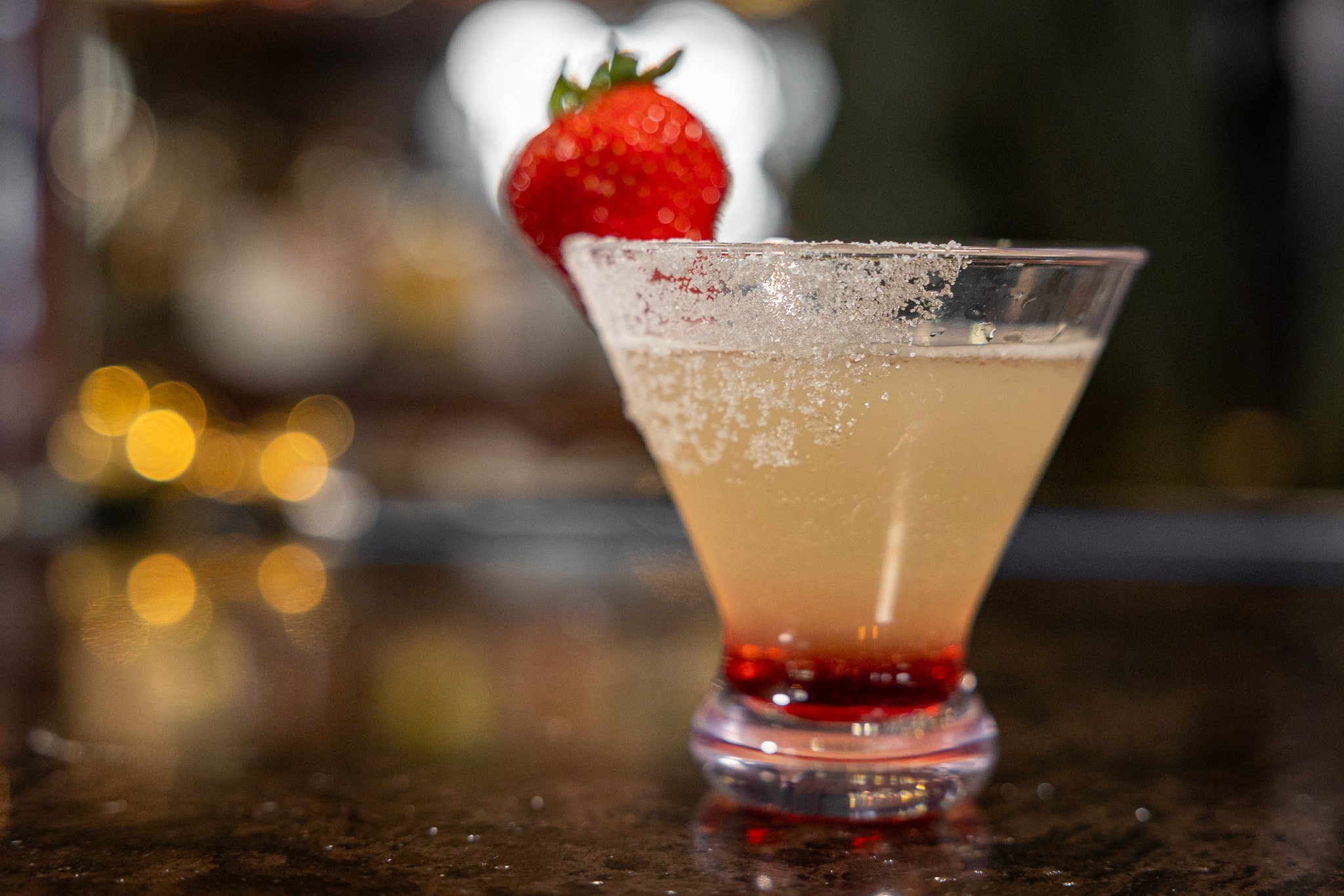 short martini glass filled with strawberry mango lemon drop. glass has a sugar rim & strawberry garnish