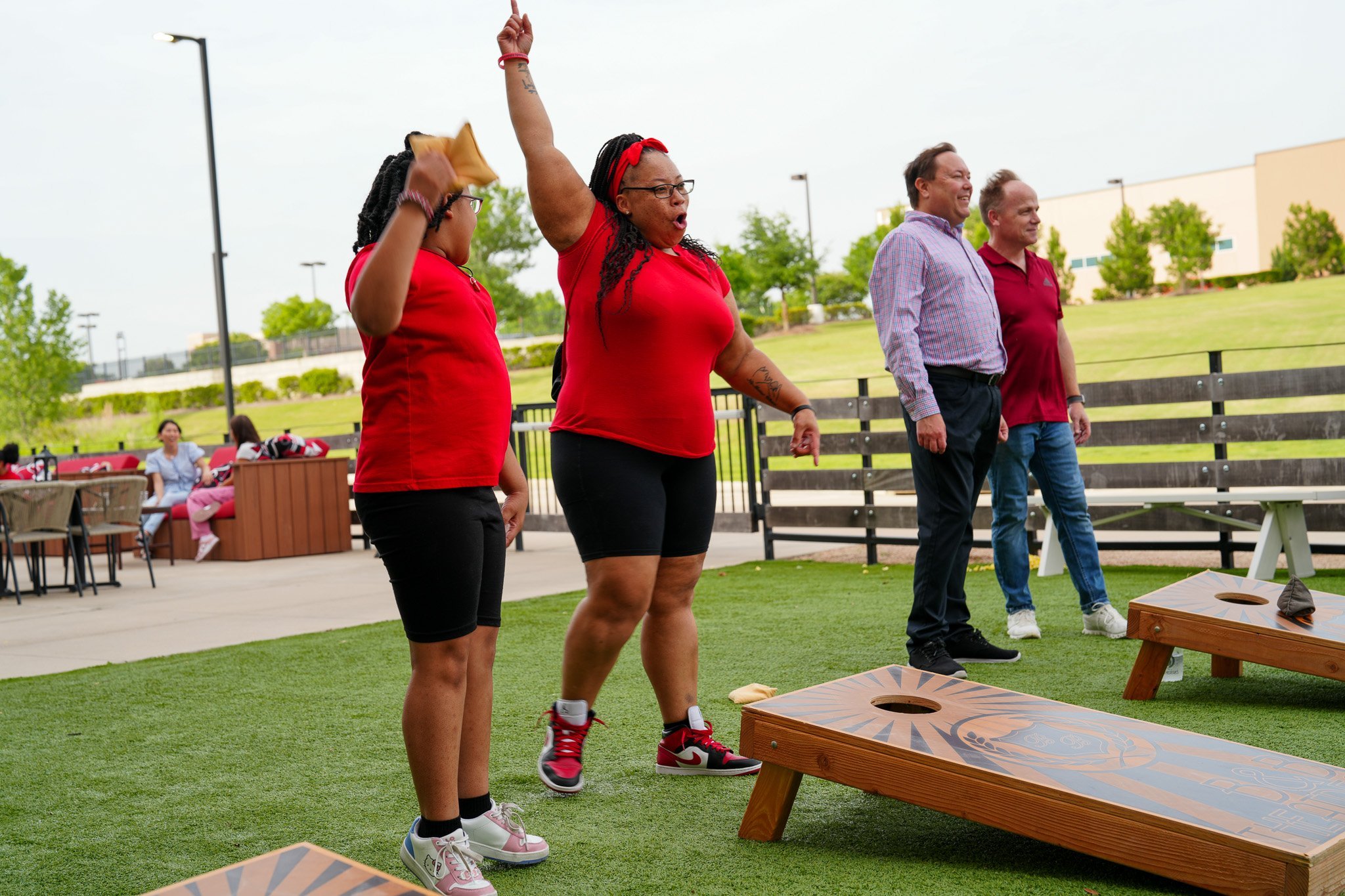4 guests outside playing cornhole. 1 woman with her arm up cheering
