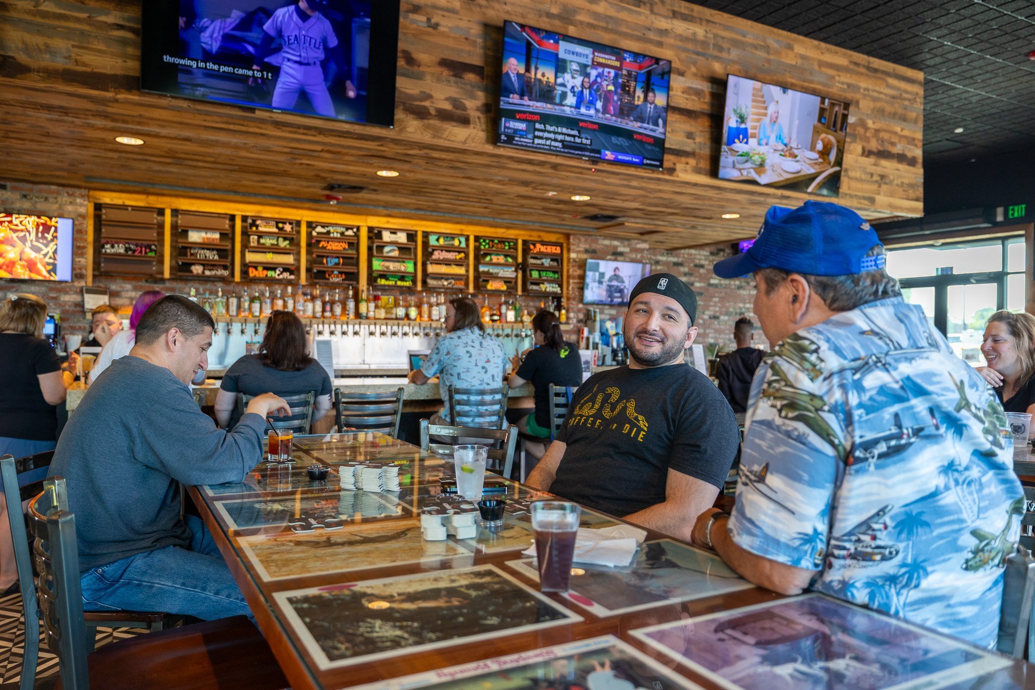 3 men sitting at table in bar area. Glasses of drinks sit on the table in front of them