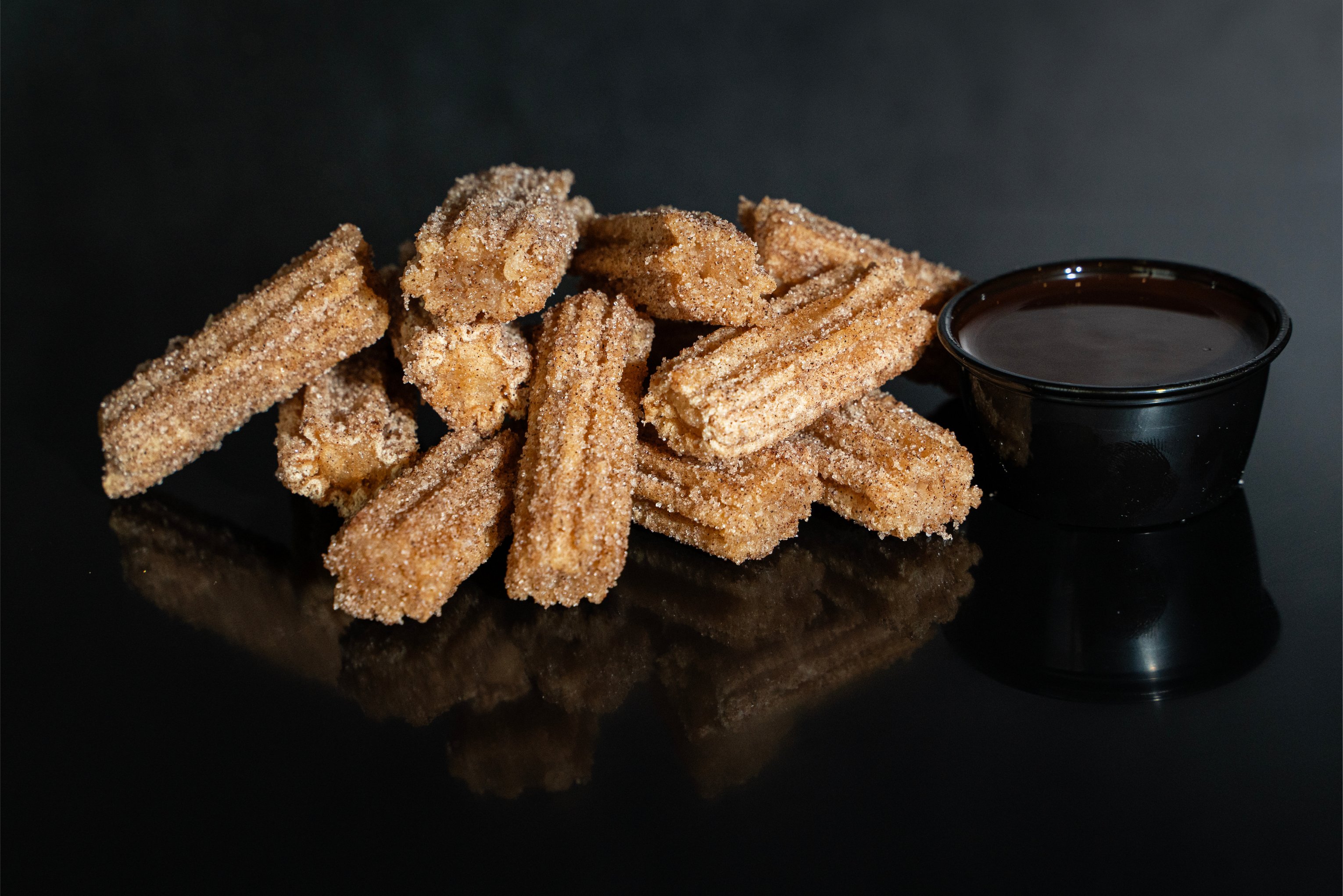 pile of churro bites with cup of chocolate sauce to the right side