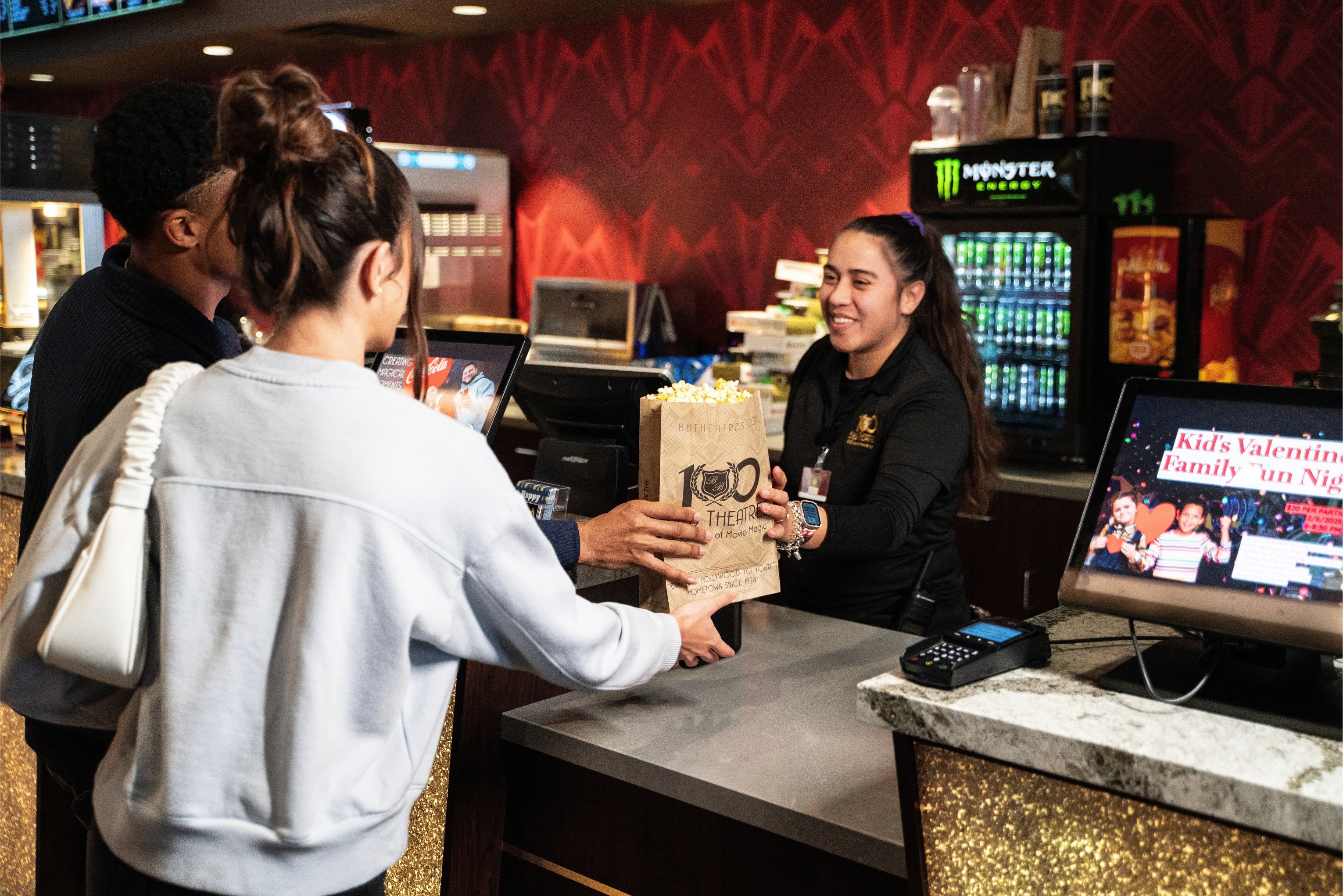 man and woman receiving a bag of popcorn from a concession stand employee