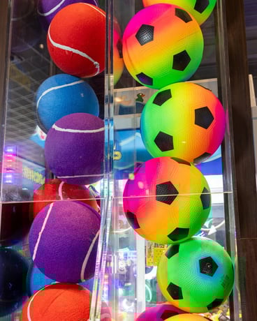 2 tall prize towers side-by-side. One side holds giant colorful tennis balls, the other holds multi-colored soccer balls