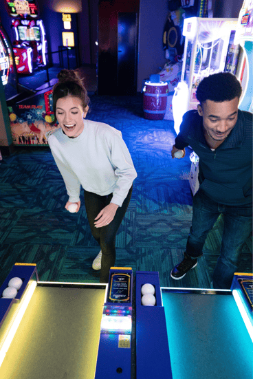 a woman and man are getting ready to throw a skee-ball. both have excited happy looks on their faces.