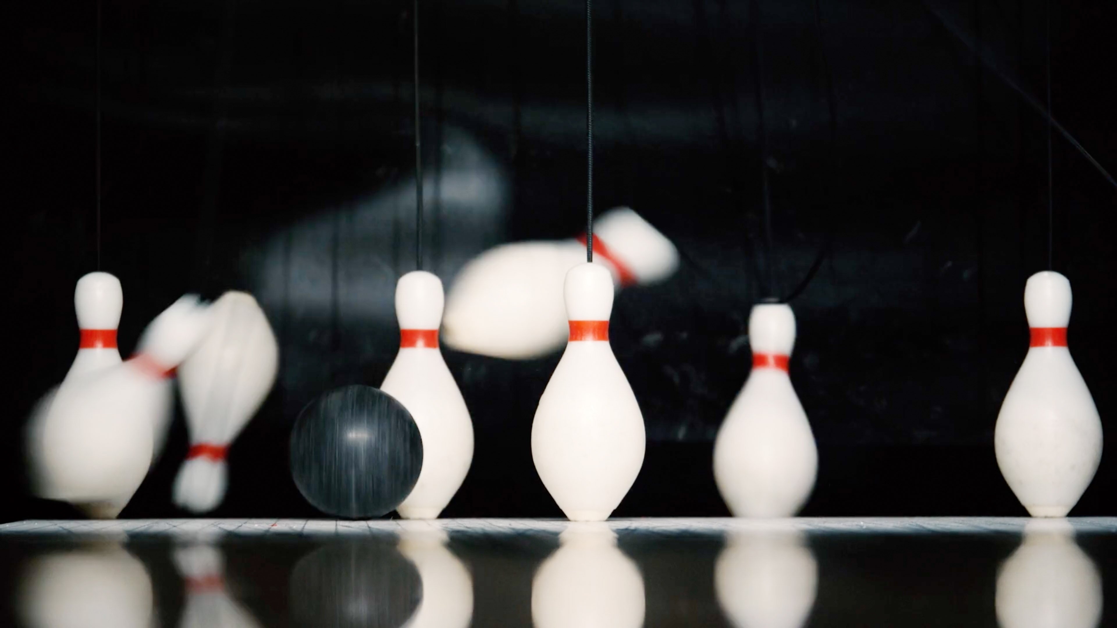 small black duckpin ball rolling into pins. some pins falling over