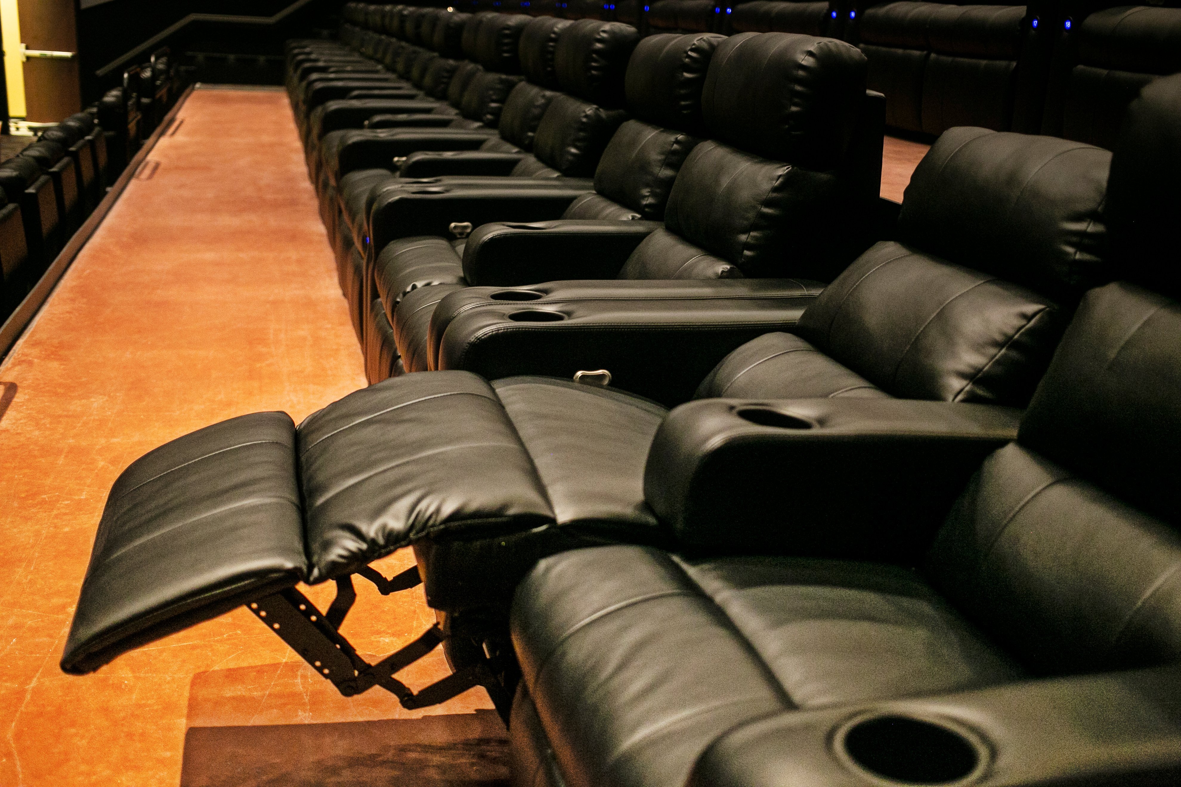 row of black recliners. 1 seat is reclined