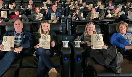 auditorium full of guests with popcorn and drinks smiling at movie screen