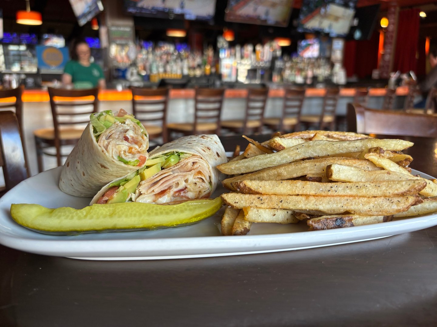 White plated filled with cali wrap, stack of fries, and pickle spear