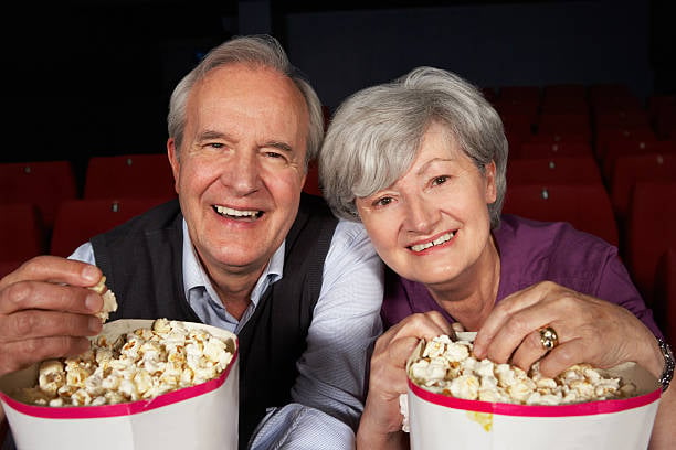 Older male and female smiling and eating popcorn