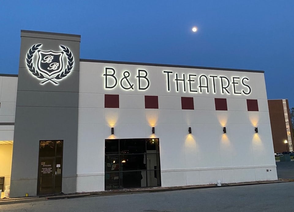 exterior of building during early evening. Moon is in the sky. The building has lit signage that is the B&B Logo and large black letters that reads: B&B Theatres